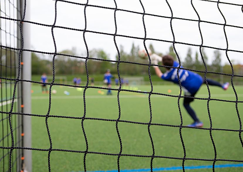 Torwart Kind springt nach dem Ball, Ansicht von hinter dem Tornetz