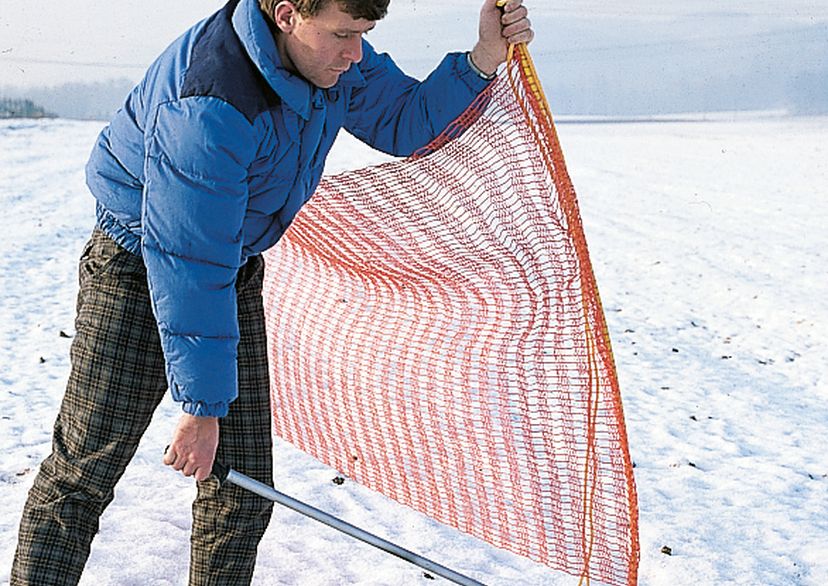 Man zieht Bodenhülse raus für Schneefangzaun, Bild im Freien (im Schnee)