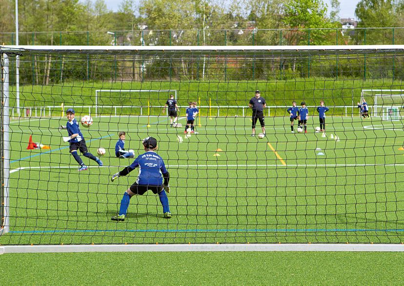 Kinder-Fußballtraining mit Trainer, Blick von hinter dem Tornetz